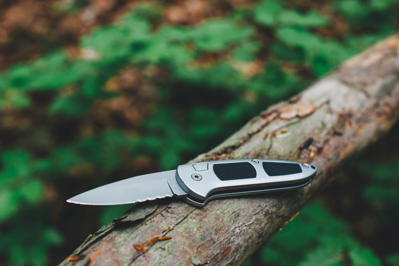 A stainless steel folding knife resting on a wooden log